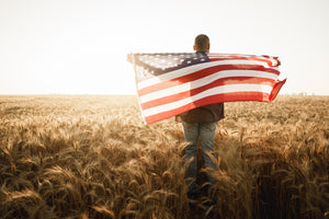 Man walking through a field holding an American Flag
